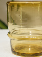 Load image into Gallery viewer, A close-up of a translucent amber yellow glass cup with a flared rim, resting on a white textured surface.
