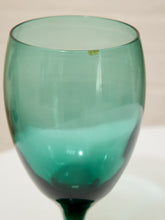 Load image into Gallery viewer, A translucent teal green glass goblet or wine glass with a dark green base, shown against a light beige background.