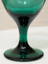 Load image into Gallery viewer, A close-up of a translucent green glass goblet or tumbler with a wide circular base, showing dark green to black shading from the glass thickness and lighting.