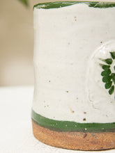 Load image into Gallery viewer, Close-up of a handmade ceramic mug with a speckled off-white glaze, a green band near the base, and a rustic brown unglazed foot.