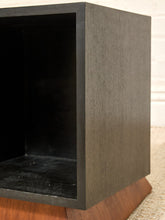 Load image into Gallery viewer, Close-up of a dark charcoal gray wooden cube side table or shelf with a visible wood grain finish, set on a wooden base over a light textured rug.