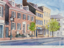 Load image into Gallery viewer, Watercolor painting of a street scene featuring historic brick and yellow buildings, green trees, black street lamps, and a blue sky. The artwork is signed in the lower right corner.