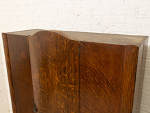 Load image into Gallery viewer, A close-up of a dark brown wooden cabinet with a wavy top edge, set against a white painted brick wall.