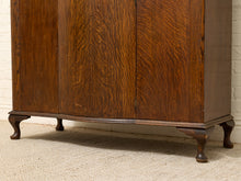 Load image into Gallery viewer, A close-up of a dark brown wooden cabinet with a prominent grain pattern, featuring three front doors and curved cabriole-style legs, set against a white brick wall and beige carpet.