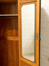 Load image into Gallery viewer, A wooden wardrobe or closet door with a large rectangular mirror inset, set against a white brick wall.