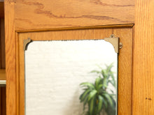 Load image into Gallery viewer, A close-up of a vintage wooden cabinet or dresser featuring a rectangular mirror with brass corner brackets.