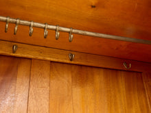 Load image into Gallery viewer, Close-up of a rustic wooden cabinet or wardrobe interior with a metal hanging rod across the top and several small metal hooks on the front.