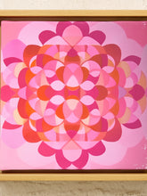 Load image into Gallery viewer, A square framed abstract artwork featuring a symmetrical floral or mandala-like pattern in shades of pink, coral, orange, and magenta, set in a light wood frame against a light textured wall.