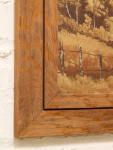 Load image into Gallery viewer, Close-up of a framed landscape painting showing a golden-brown field with a rustic fence and trees, bordered by a thick warm wood frame against a white textured wall.