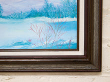 Load image into Gallery viewer, A close-up of a framed winter landscape painting, showing a snowy blue scene with dark trees and pinkish reeds, mounted on a textured off-white wall.