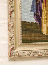 Load image into Gallery viewer, Close-up of an ornate carved wooden picture frame with distressed gold and beige tones, mounted on a white painted brick wall. A portion of a needlepoint or embroidered artwork is visible inside the frame.
