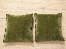 Load image into Gallery viewer, Two square olive green velvet throw pillows placed side by side on a beige woven jute rug.