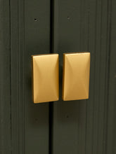 Load image into Gallery viewer, Two rectangular gold cabinet knobs with a beveled geometric edge, mounted on dark green paneled doors.