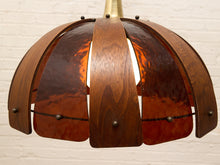 Load image into Gallery viewer, A mid-century modern pendant light with a dome-shaped shade made of curved dark brown wood slats and translucent amber glass panels, suspended from a brass rod against a white brick wall.