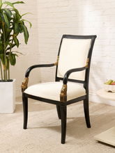 Load image into Gallery viewer, Vintage Neoclassical armchair featuring ivory upholstery, a black wood frame, sculpted arms, and ornate gold-tone carved details.