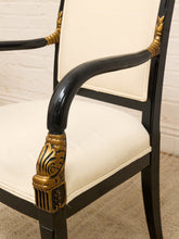 Load image into Gallery viewer, Close-up of an armchair with cream-colored upholstered seat and backrest, a glossy black frame, and ornate gold decorative accents on the armrests and leg.