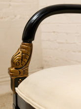 Load image into Gallery viewer, Close-up of a black wooden chair arm with an ornate gold metal decorative cap and a cream-colored fabric cushion, set against a white brick wall background.