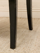 Load image into Gallery viewer, Close-up of a black wooden table leg standing on a textured beige rug against a white brick wall.