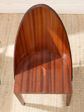 Load image into Gallery viewer, A high-back wooden chair with a curved, shell-like backrest and a thick seat, crafted from rich reddish-brown wood with visible grain, set on a woven beige rug.