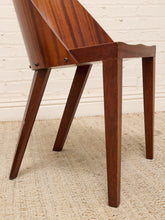Load image into Gallery viewer, A close-up of a mid-century modern wooden chair with a rich dark brown grain, featuring angled legs and a minimalist backrest, set against a white brick wall and beige rug.