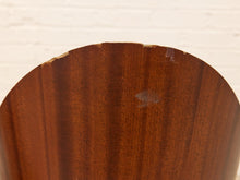 Load image into Gallery viewer, Close-up of a curved wooden object, likely a chair back or stool backrest, made of medium-to-dark brown wood with visible grain and minor wear or scuffs near the top edge, set against a white painted brick wall background.