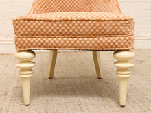 Load image into Gallery viewer, A close-up of an upholstered ottoman or stool with a peach and beige checkered pattern on the seat cushion and backrest, supported by four turned cream-colored wooden legs.
