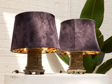 Load image into Gallery viewer, Two matching table lamps with dark purple velvet drum shades and distressed bronze bases, displayed on a white surface against a white brick wall with green leaves in the background.