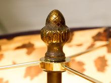 Load image into Gallery viewer, Close-up of a decorative brass lamp finial shaped like an acorn or pine cone, mounted on a lamp post with a patterned shade blurred in the background.