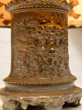 Load image into Gallery viewer, Close-up of an ornate bronze-toned metal container or vessel with a sculpted face motif and decorative ridged rim, shown against a softly blurred neutral background.