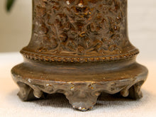 Load image into Gallery viewer, Close-up of an ornate bronze-colored metal base with intricate floral relief carvings and a tiered footed stand, resting on a light fabric surface.