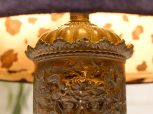 Load image into Gallery viewer, Close-up of an ornate carved lamp base in a metallic gold and bronze finish, with a patterned fabric shade visible in the background.