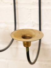 Load image into Gallery viewer, A close-up of a brass wall-mounted candelabra holder with a circular flared top and a dark metal hanging arm against a white brick wall.