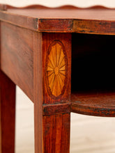 Load image into Gallery viewer, Close-up of a dark reddish-brown wooden table corner featuring a decorative oval sunburst inlay on the leg, with a dark shelf opening and a light neutral floor background.