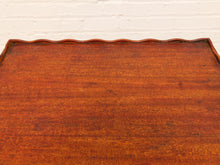 Load image into Gallery viewer, Close-up of a polished reddish-brown wooden surface with a wavy scalloped edge, set against a white painted brick wall.