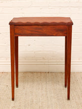 Load image into Gallery viewer, A small wooden side table with a scalloped apron front and four tapered legs, shown against a white painted brick wall and light woven rug.