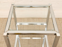 Load image into Gallery viewer, A square side table with a clear glass top and polished silver metal frame, shown from a top-down angle on a beige carpeted floor.