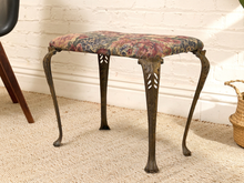 Load image into Gallery viewer, A vintage-style upholstered stool with a floral patterned seat cushion and dark carved cabriole legs, set on a beige rug against a white brick wall.
