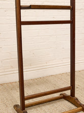Load image into Gallery viewer, A vintage wooden ladder-style coat rack with a warm brown finish, standing on a textured beige rug against a white brick wall.