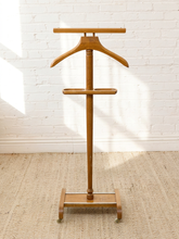 Load image into Gallery viewer, A wooden garment stand with a hanger and shelf, photographed indoors against a white brick wall on a beige rug.