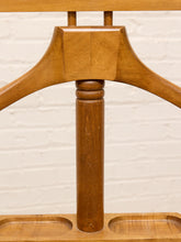 Load image into Gallery viewer, Close-up of a warm medium-brown wooden chair frame, showing the central vertical post and curved side supports against a white painted brick wall background.