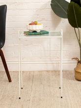Load image into Gallery viewer, Vintage white-painted metal tray table with rectangular clear glass top, slender legs, raised frame, and curved side handles
