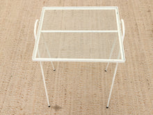 Load image into Gallery viewer, A white metal serving table with a clear glass top and two loop handles on the sides, shown on a textured beige woven rug.