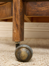 Load image into Gallery viewer, Close-up of a wooden furniture leg with a round brass caster wheel on a woven beige rug.
