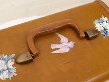 Load image into Gallery viewer, A close-up of a vintage brown leather suitcase with a distressed finish, featuring a central painted dove design, floral decals in the corners, and a weathered brown handle with brass hardware.