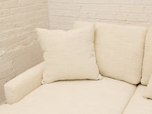 Load image into Gallery viewer, Cream-colored textured throw pillows on a matching upholstered sofa against a white brick wall.