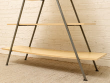 Load image into Gallery viewer, A three-tier A-frame shelving unit with light natural wood shelves and dark gray metal legs, set against a white brick wall and beige carpet.