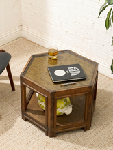 Load image into Gallery viewer, A hexagonal wooden side table with a glass top, styled in a living room corner with a notebook, a drink, and a decorative vase on it.