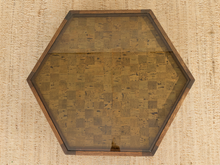 Load image into Gallery viewer, Hexagonal wooden-framed wall art with a textured, patchwork-style brown and gold surface, photographed from above on a woven beige rug.