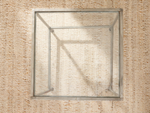 Load image into Gallery viewer, A square metal frame table top or tray with a clear glass or acrylic panel, photographed from above on a textured beige woven rug.