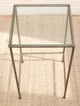 Load image into Gallery viewer, A square glass-top side table with a thin metal frame and tapered legs, shown on a woven beige rug.